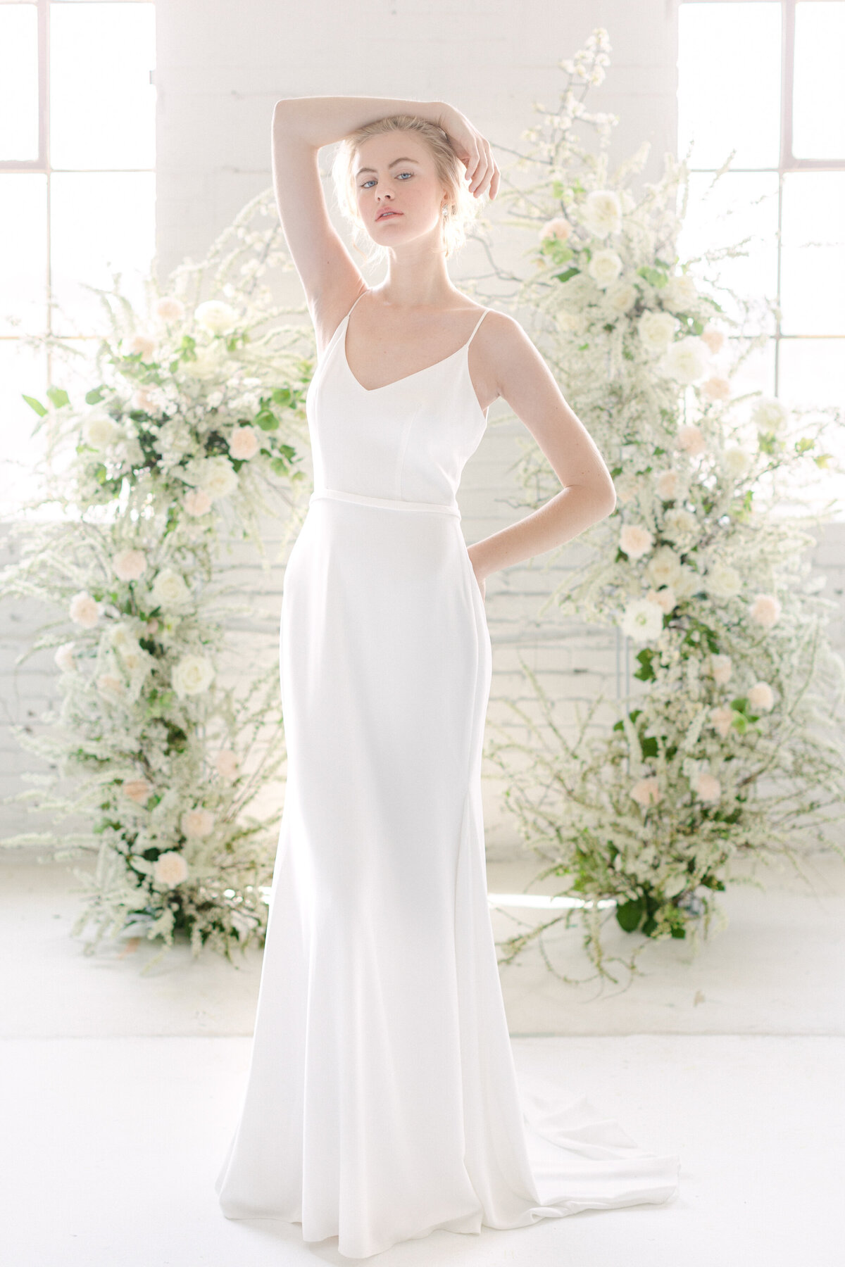 A bride poses in front of an arch of airy white flowers at a wedding at L’Eloi.