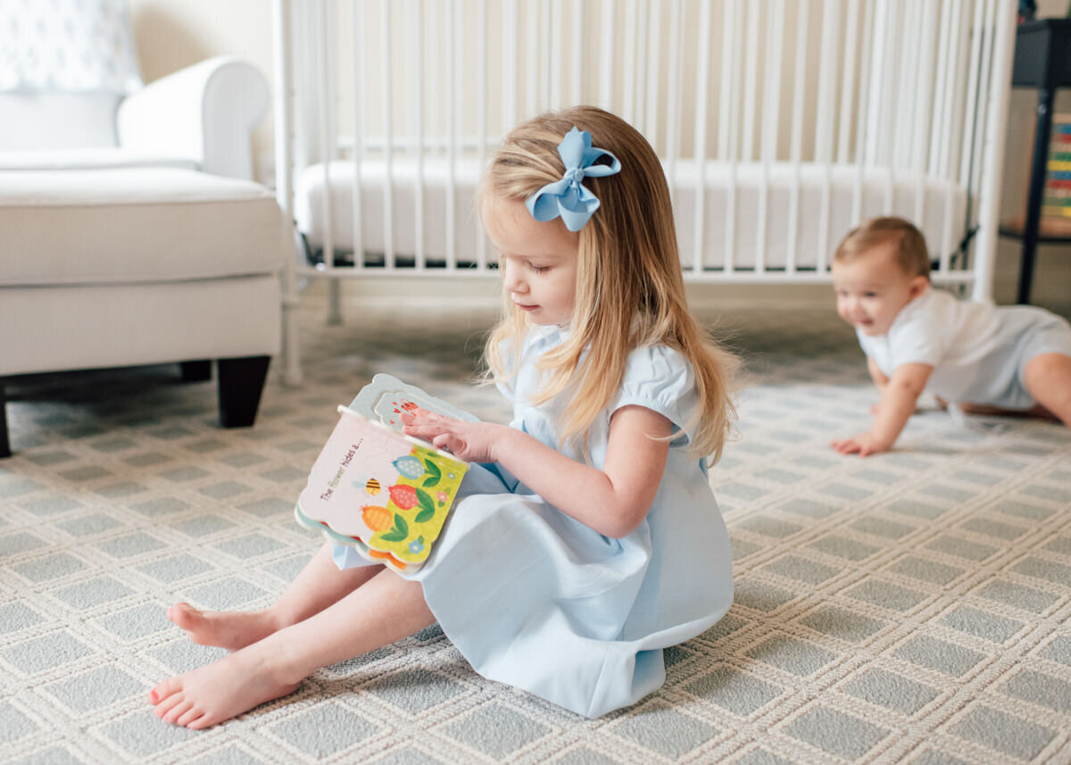 little girl reading with brother crawling