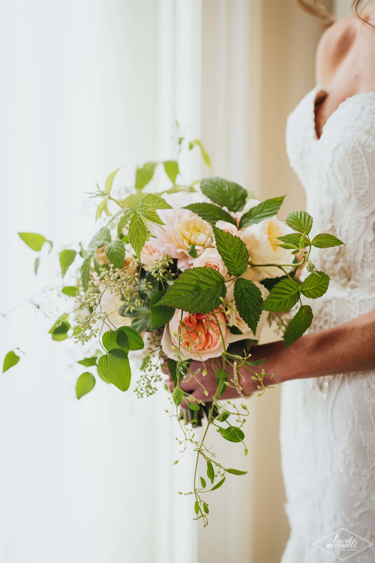 summer bridal bouquet of peach garden roses, ivory spray roses with trailing clematis vines and raspberry foliage
