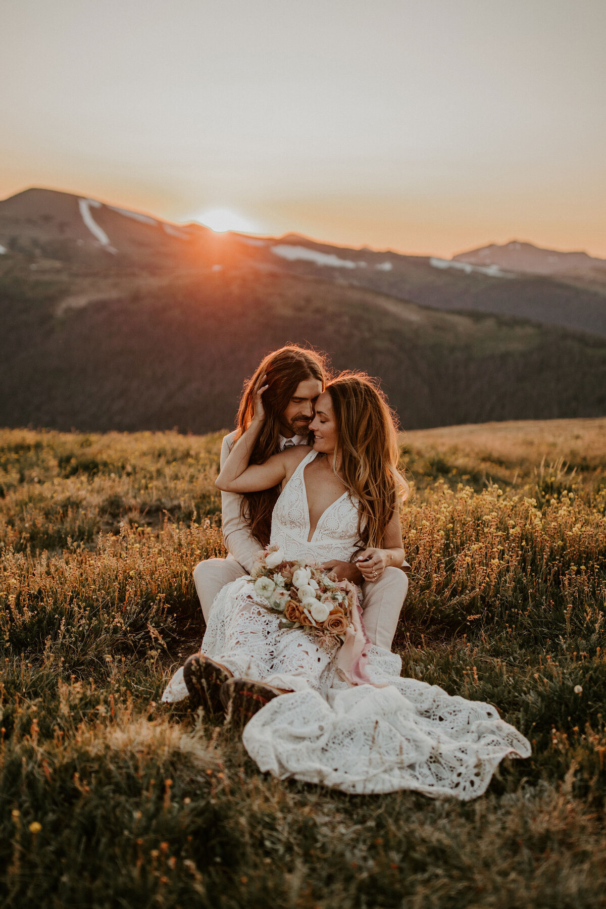 bride and groom pose holding each other at sundown in the mountains wearing a white wedding gown and ivory tuxedo