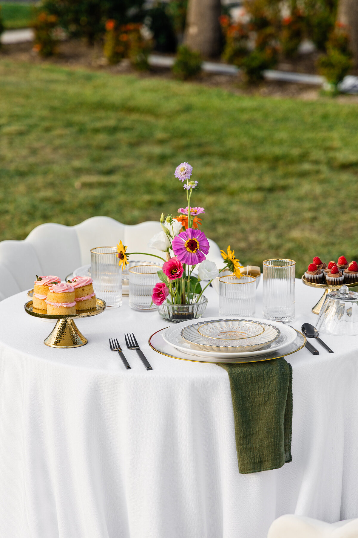 pink orange and white flowers on white table cloth with mixed metal place setting and mini chocolate and vanilla cupcakes