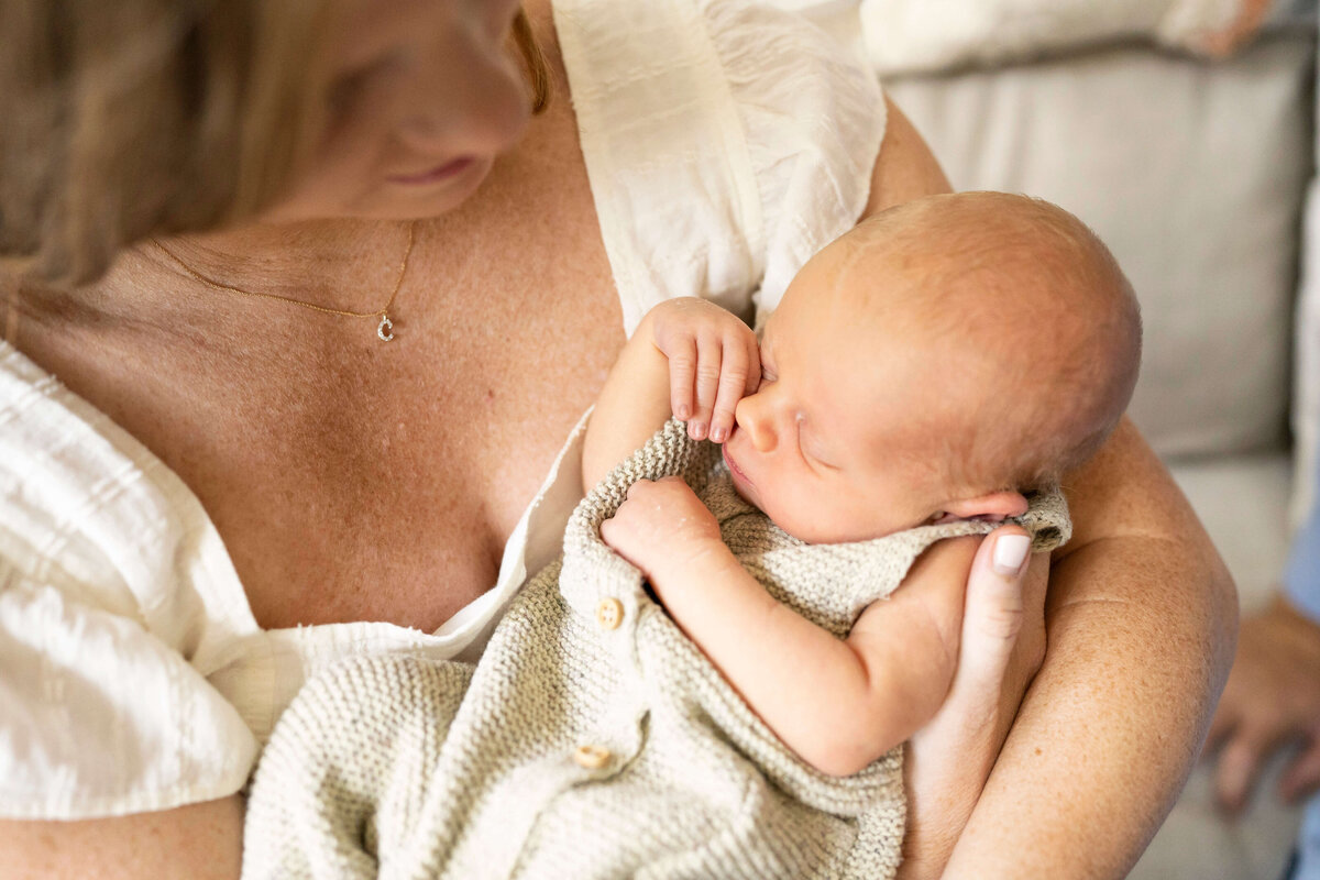 Newborn baby in tan outfit snuggled in mother's arms