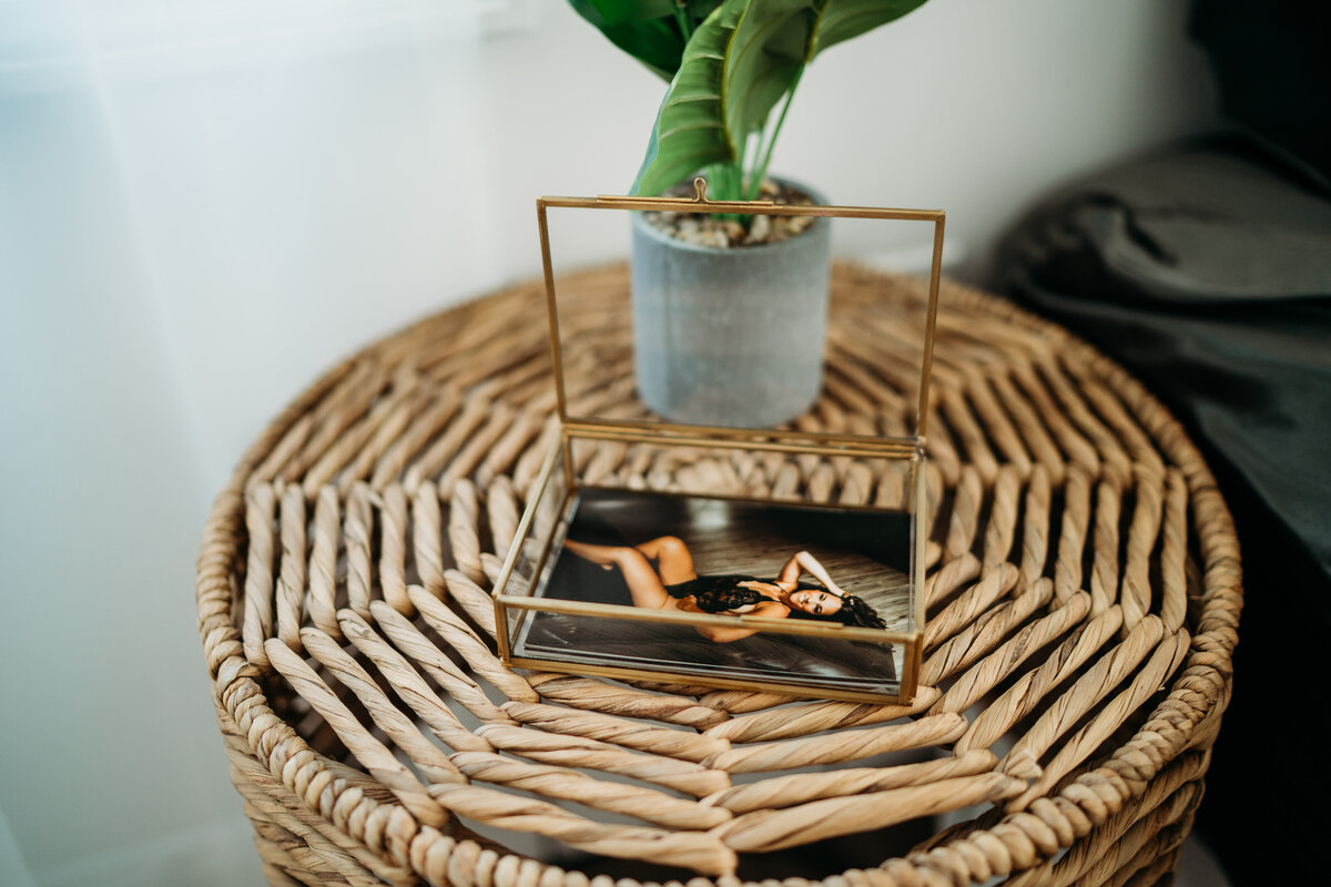 Prints of a woman in black lingerie sit in an open glass box on a wicker bedside table