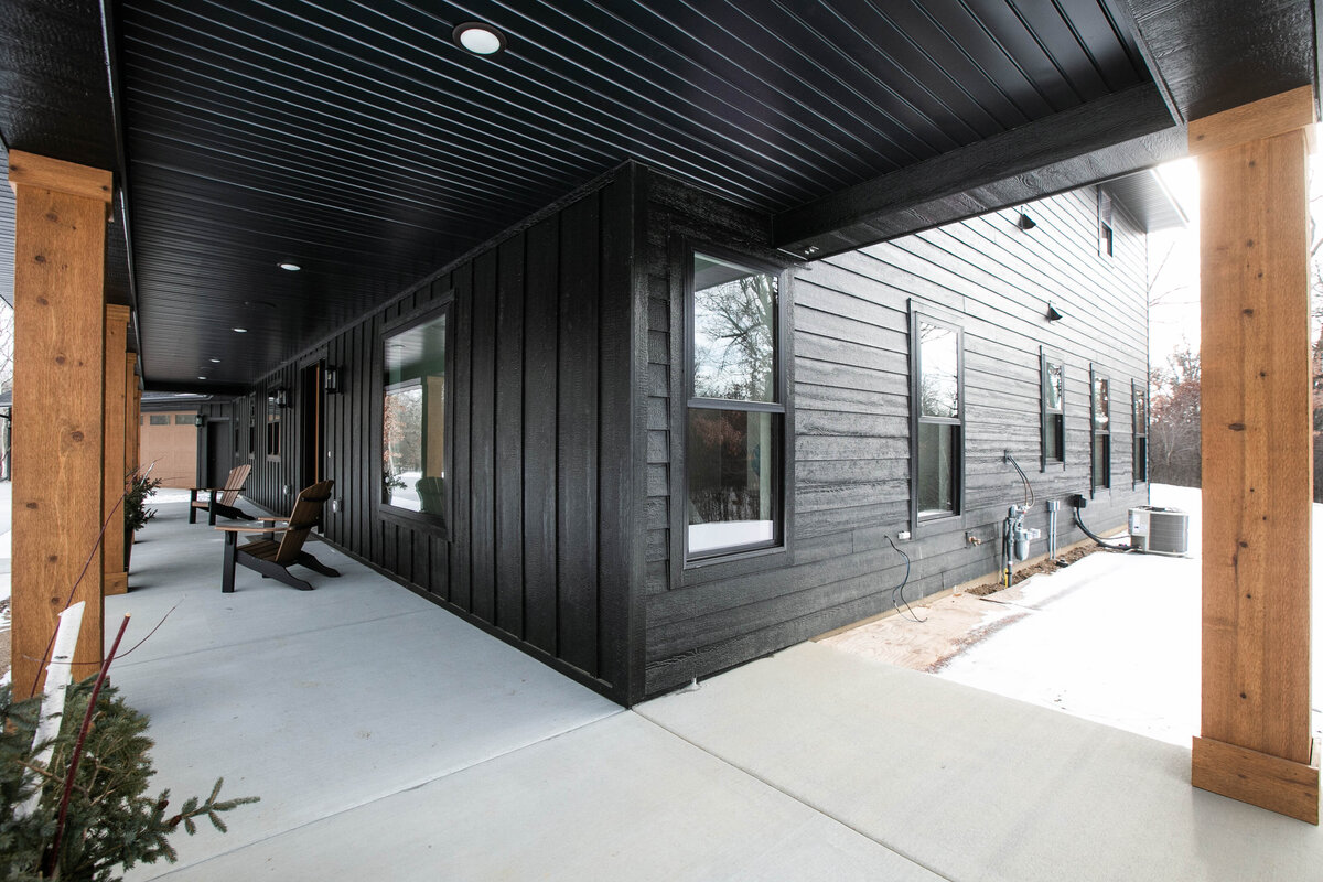 Exterior view of custom home in Elk River, Minnesota with black siding, wood details and front porch built by Cornerstone Custom Builds