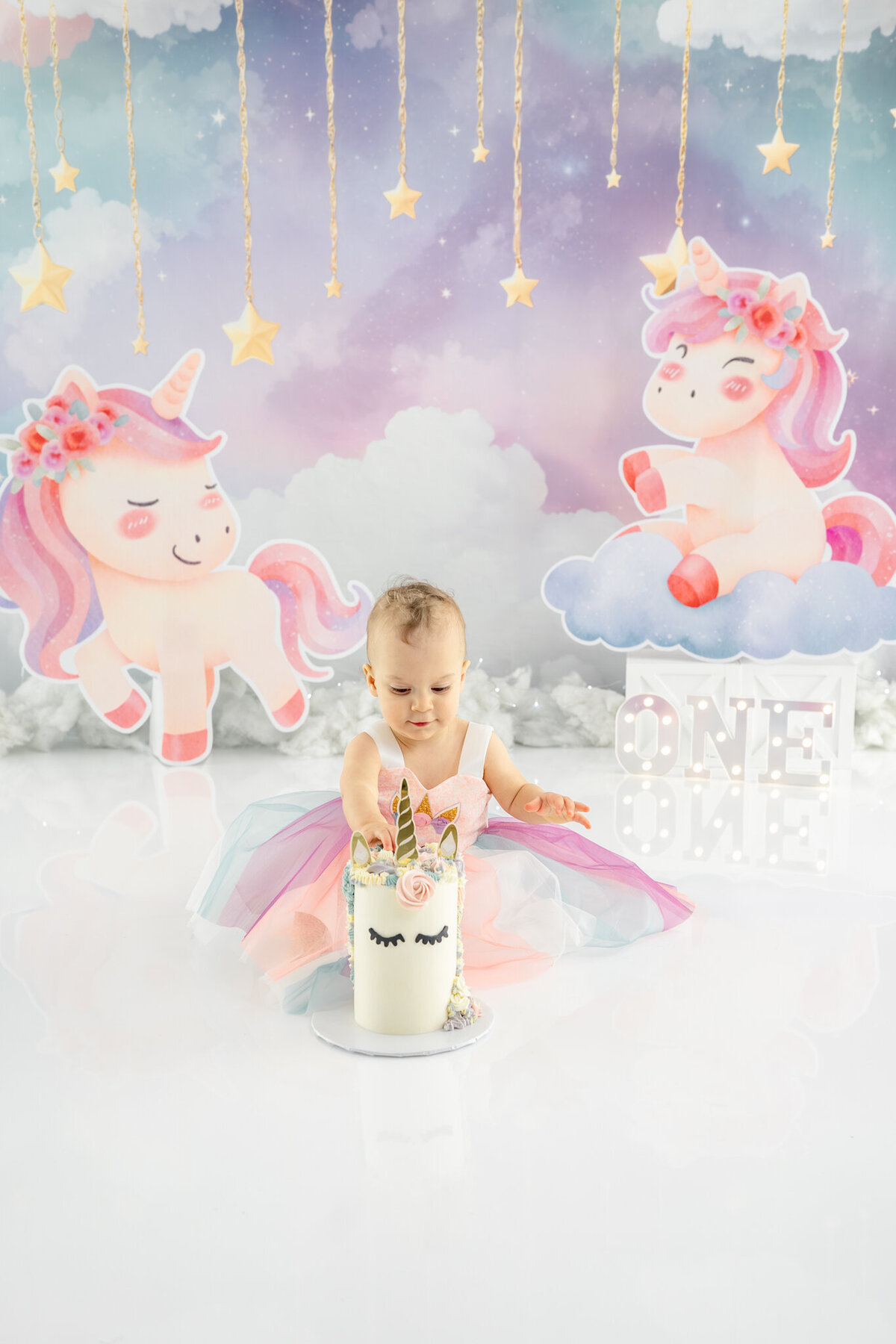 Girl in unicorn dress eating unicorn cake during themed cake smash session— captured by Alliston and Barrie cake smash photographer.