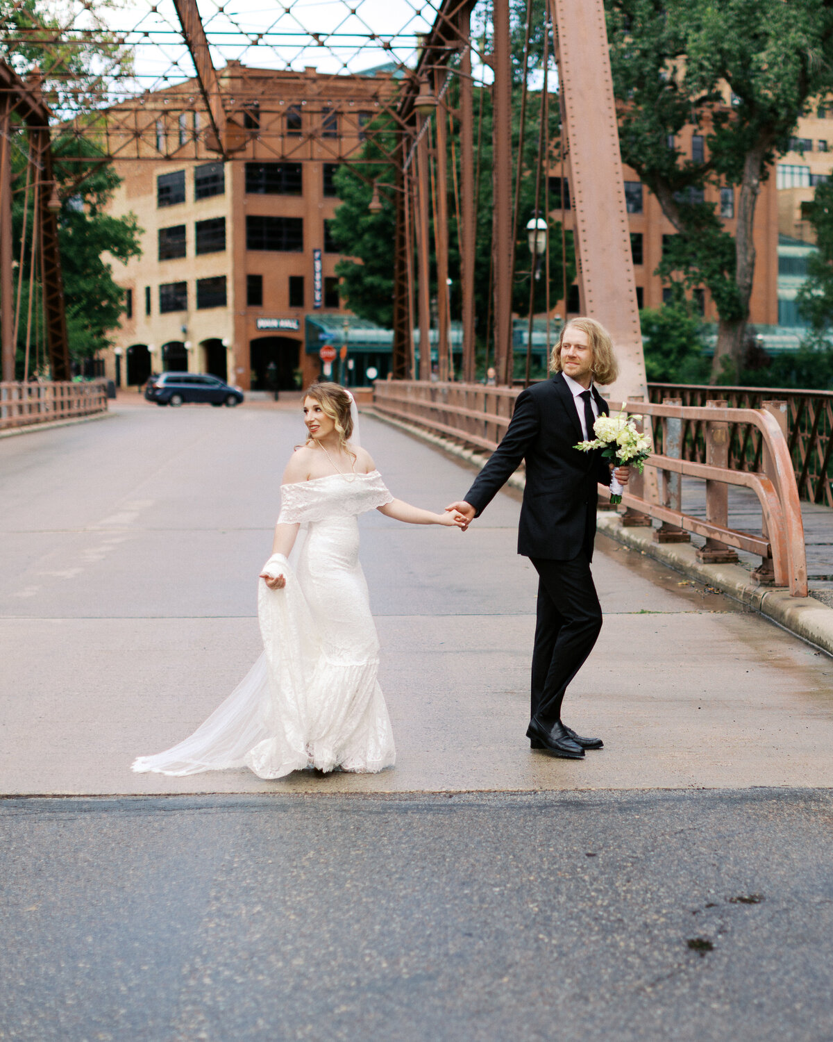 Bride and groom holding hands crossing the street with elegance in Minneapolis at Nicollet Island Inn luxury wedding.