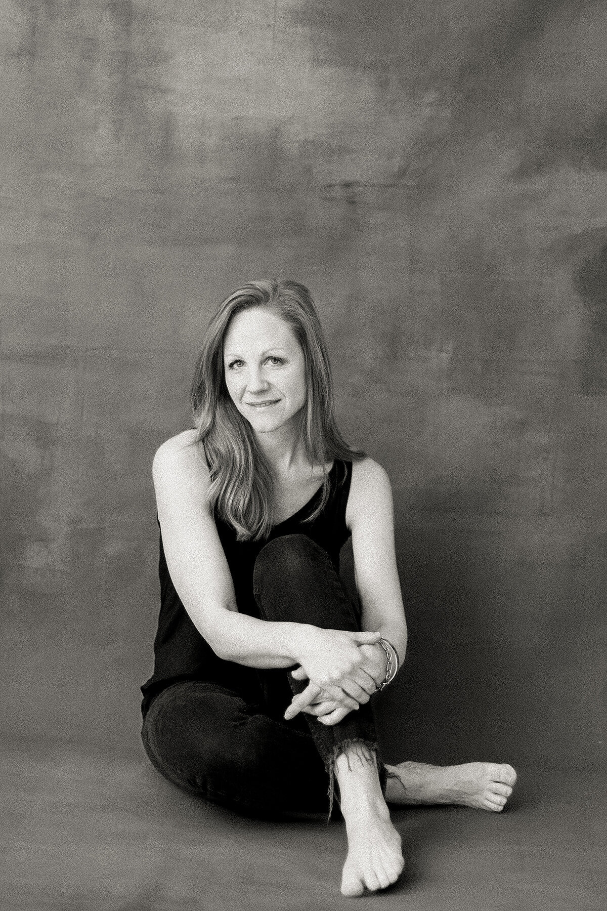 Black and white professional headshot photo of a DFW business woman sitting on the floor in a Dallas photography studio as she looks up at the photographer smiling.