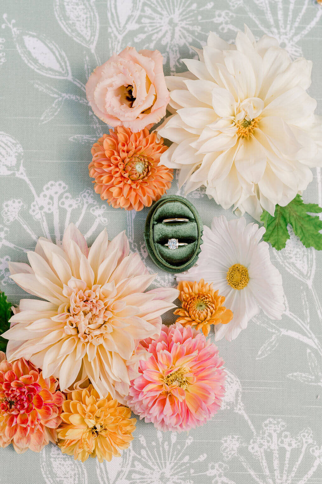 Wedding ring set in green velvet box surrounded by vibrant florals on patterned fabric.