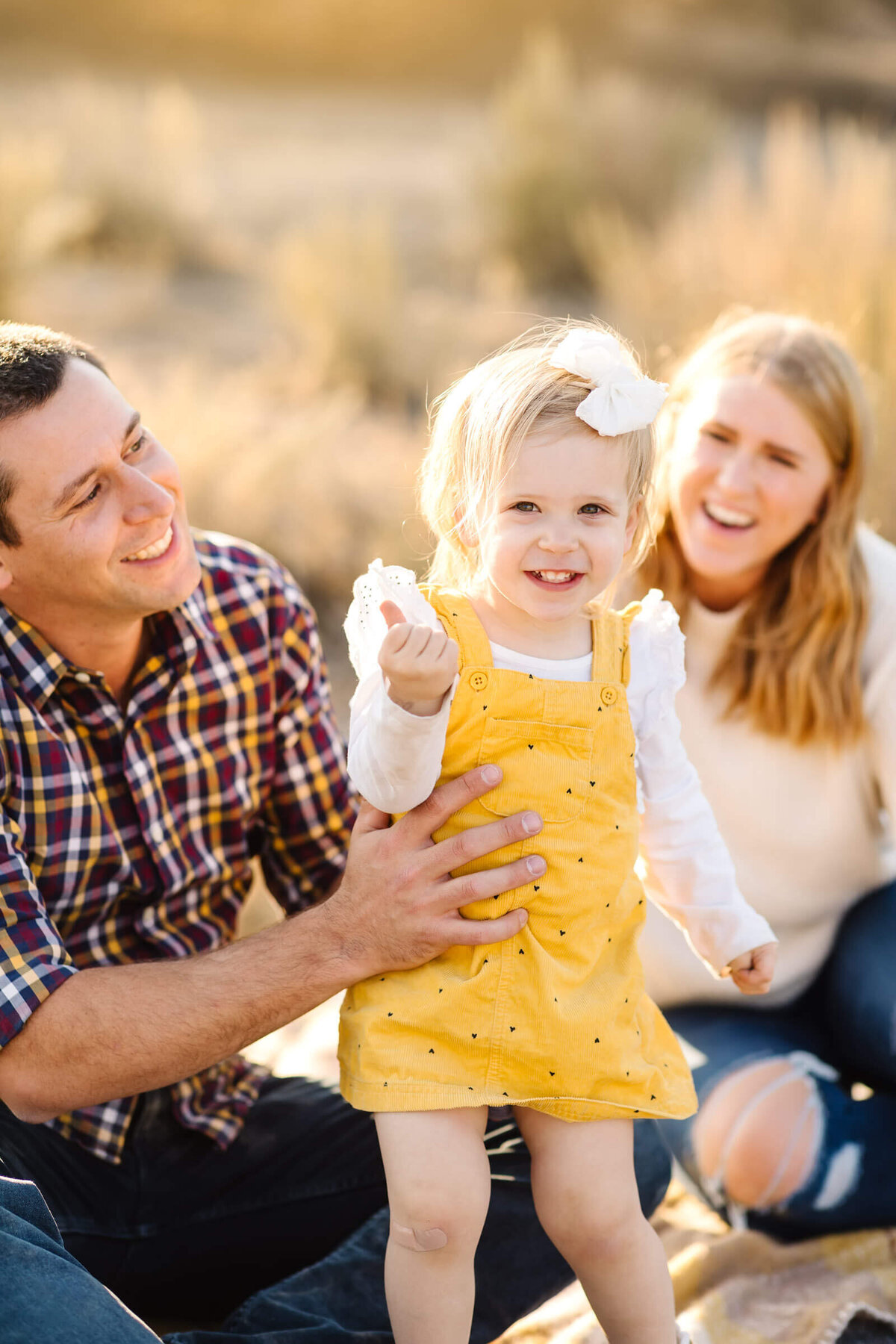 bend-family-photographer-little-blonde-girl-smiling-with-parents-looking-at-her-1