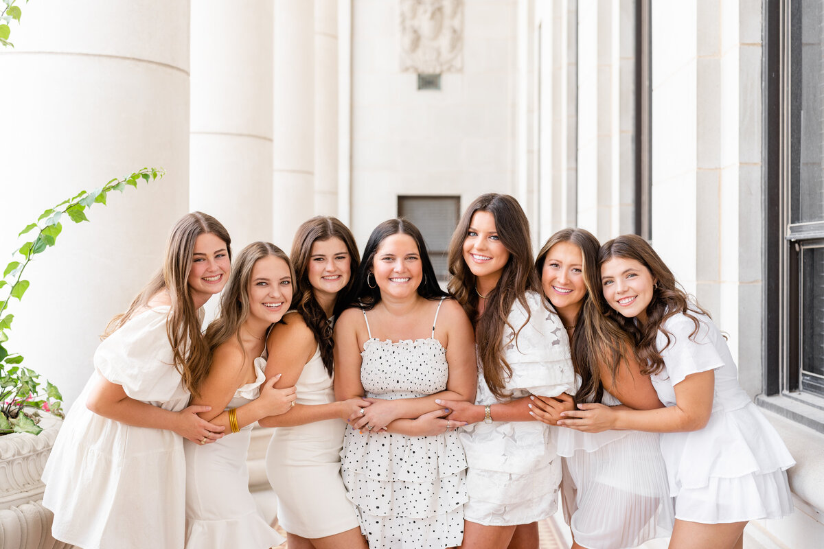 Texas A&M senior girls laughing and hugging each other while wearing white dresses in the columns of the Administration Building