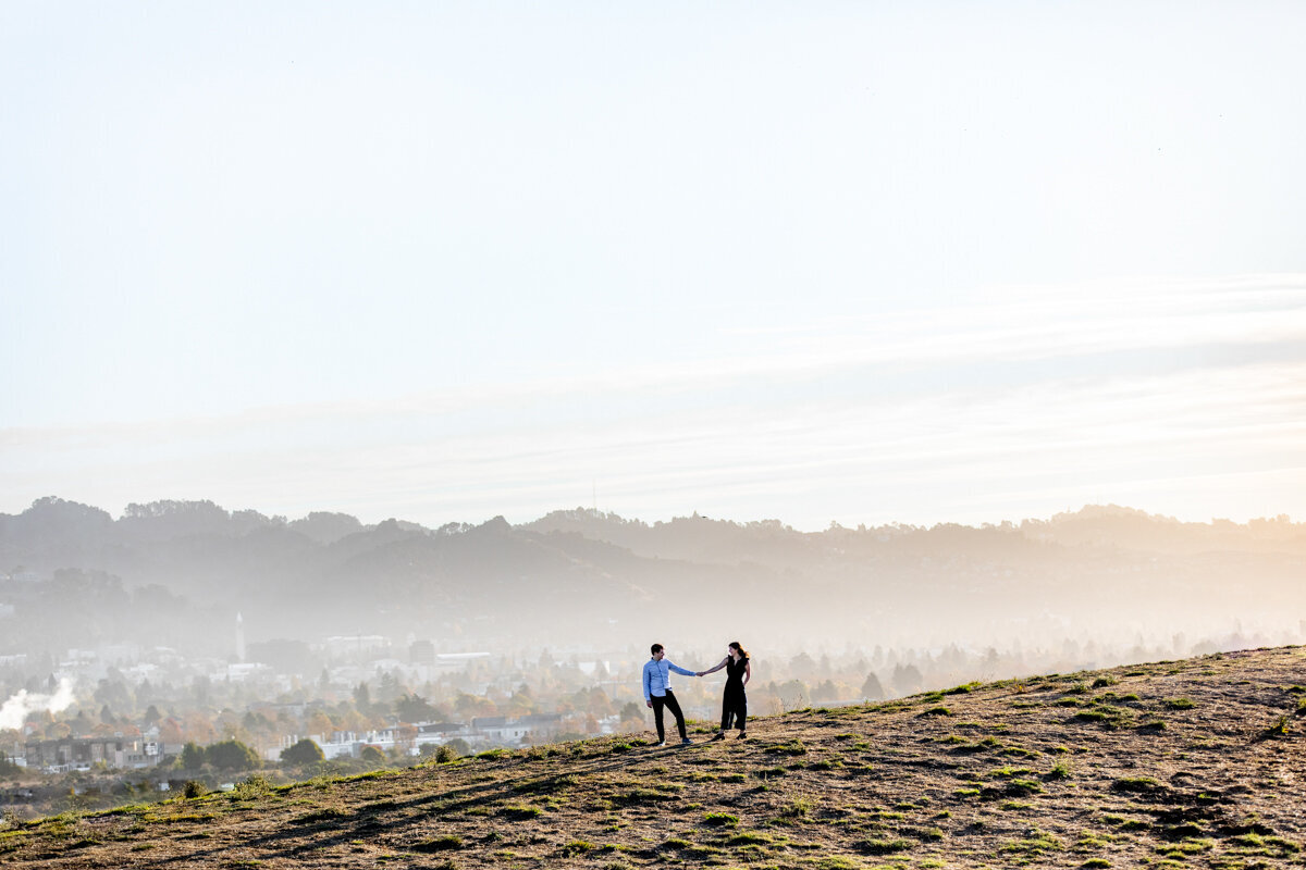 A couple holding hands while standing on the side of a large hill.