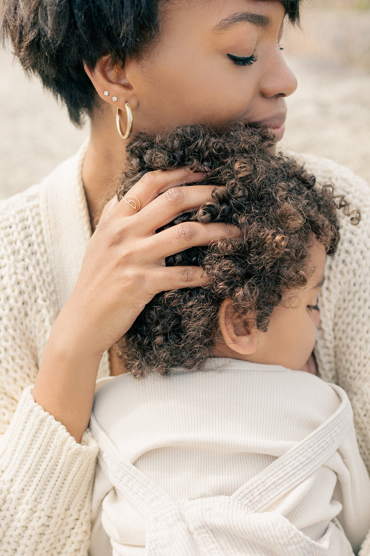 Close-up of mother running her hands through her toddler's hair while holding him close during an outdoor newborn session in Kansas City.