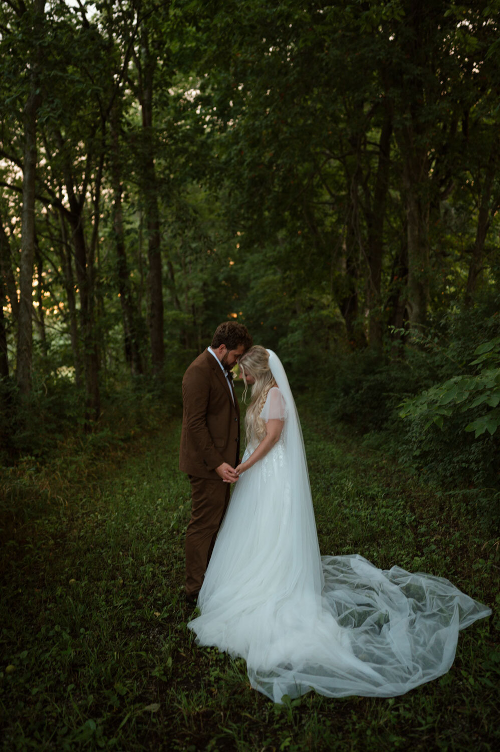 Bride and groom holding hands in a forest, gazing at each other