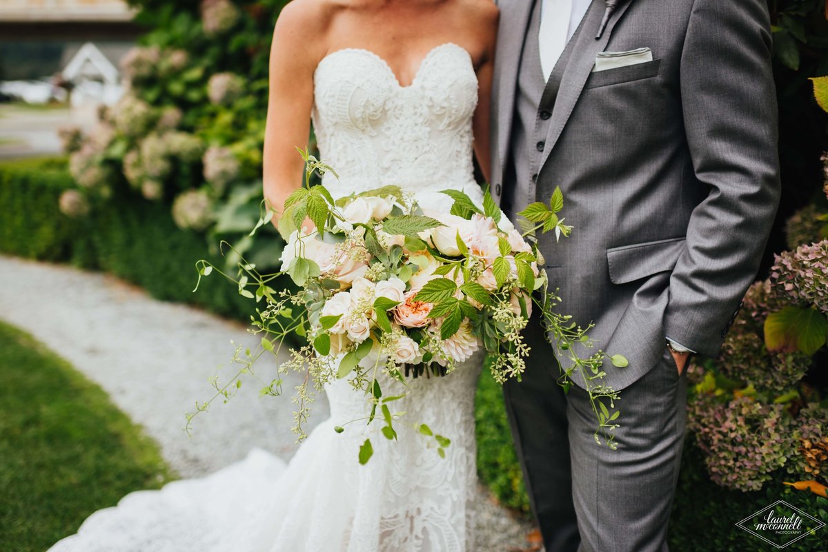 bride and groom with large bridal bouquet of Juliette gardn roses, garden spray roses, clematis vines, and raspberry foliage