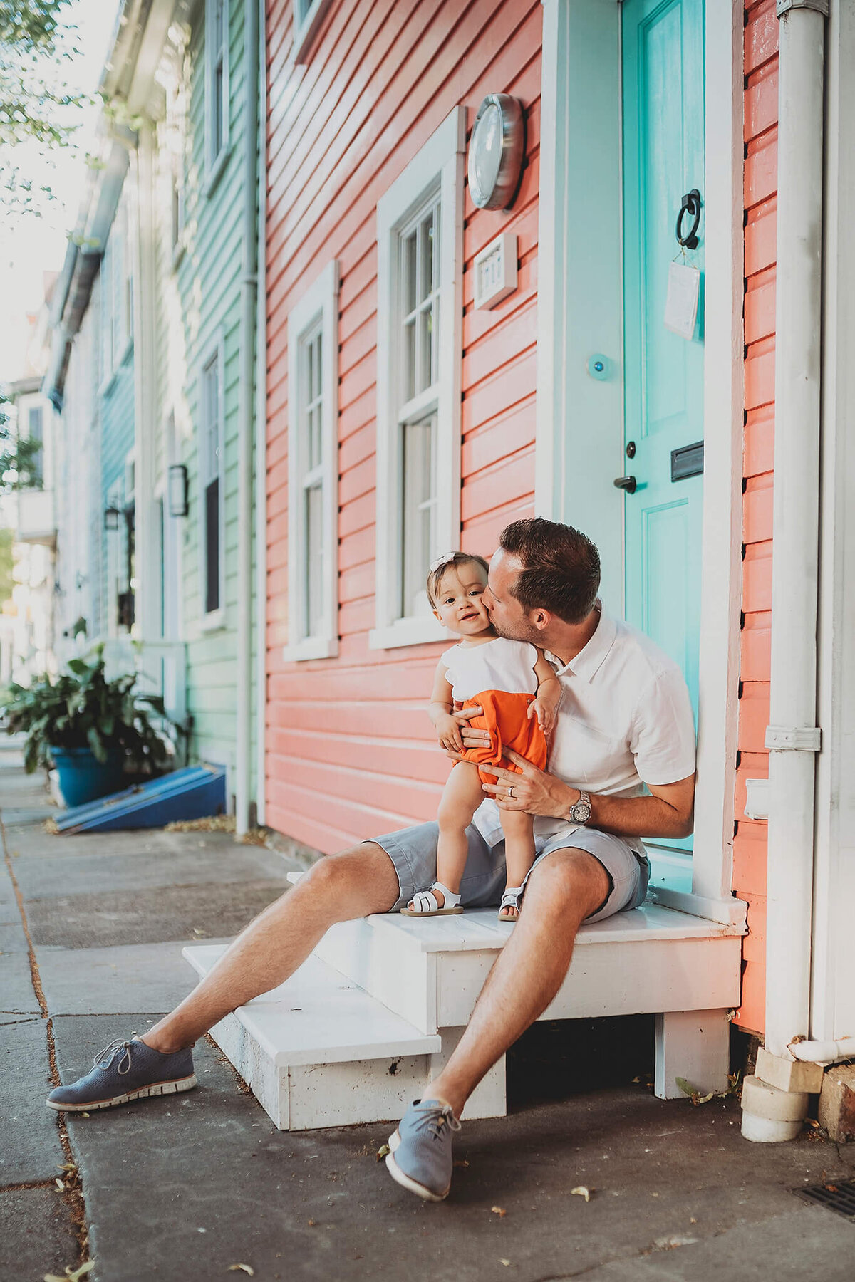 Father kissing baby in orange shorts in front of colorful houses in Fells Point Baltimore Maryland