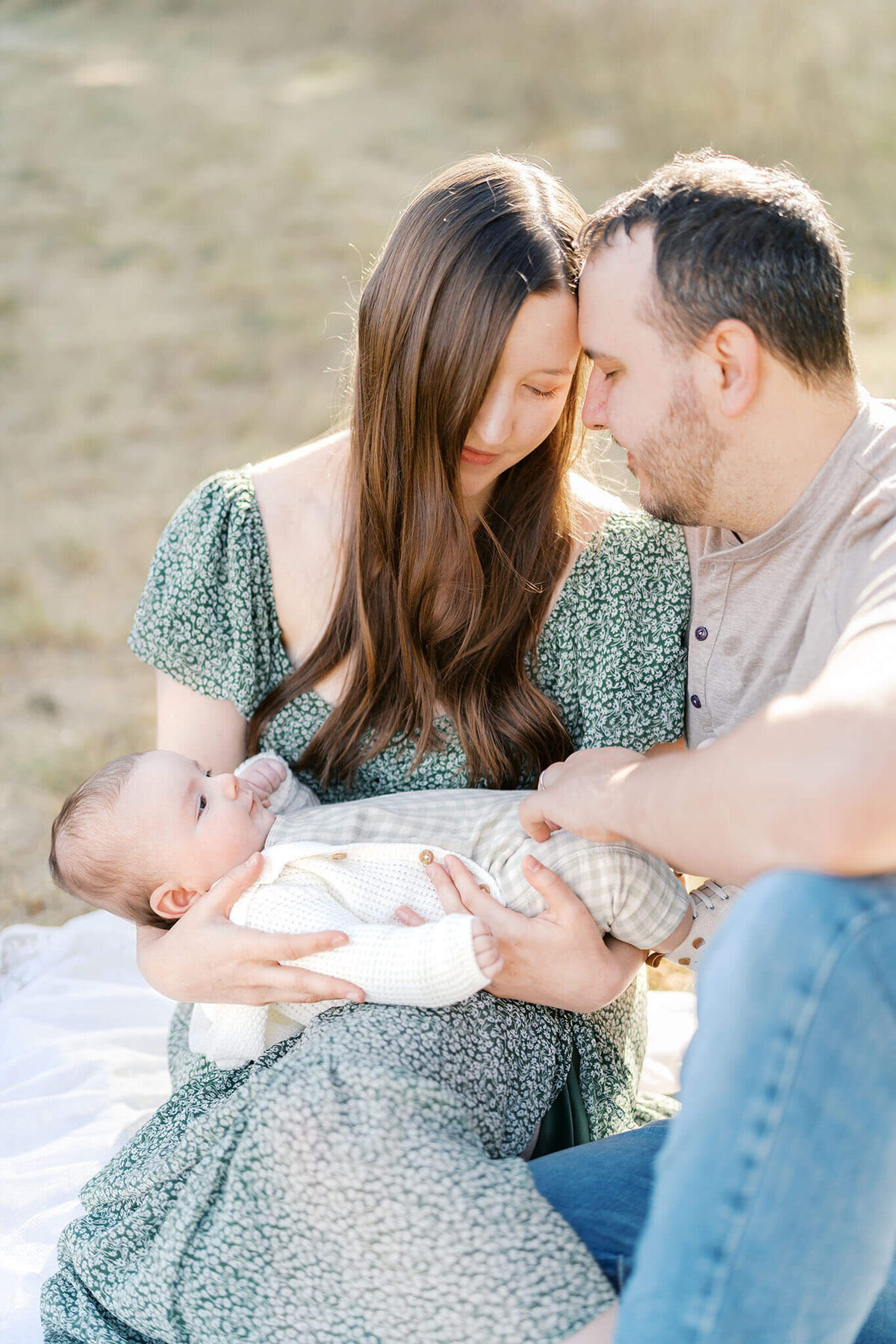 outdoor newborn photo of parents holding baby while seated on a blanket during  lifestyle newborn photos