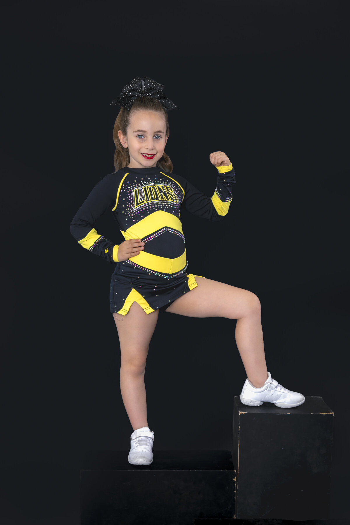 Young cheerleader posing on a black background in a strong pose showing her muscles. 