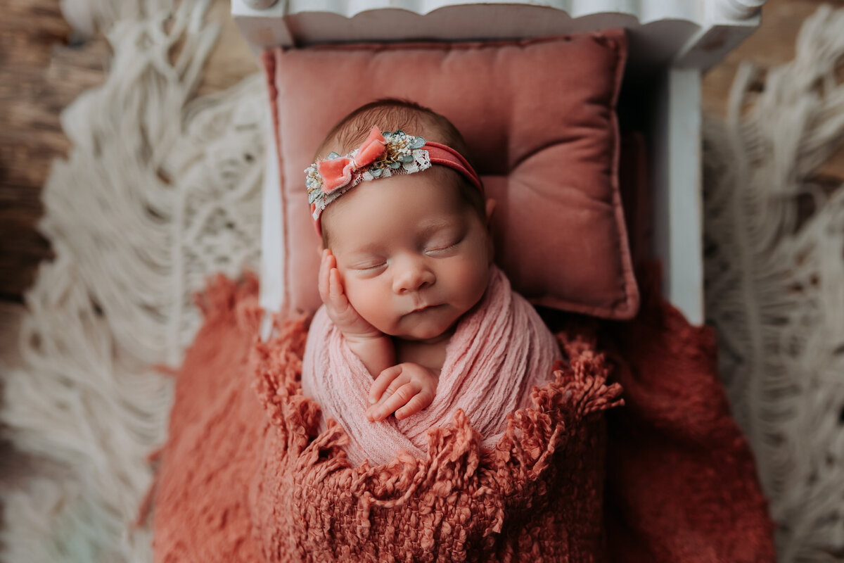 newborn girl wearing pink bow and wrapped in light pink wrap