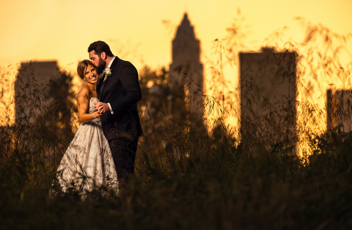 A couple holds each other as the sun sets before the Cleveland skyline.