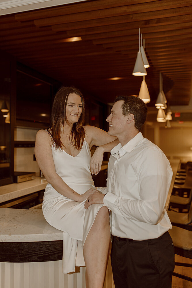 Couple sits on bar with an arm on her husband