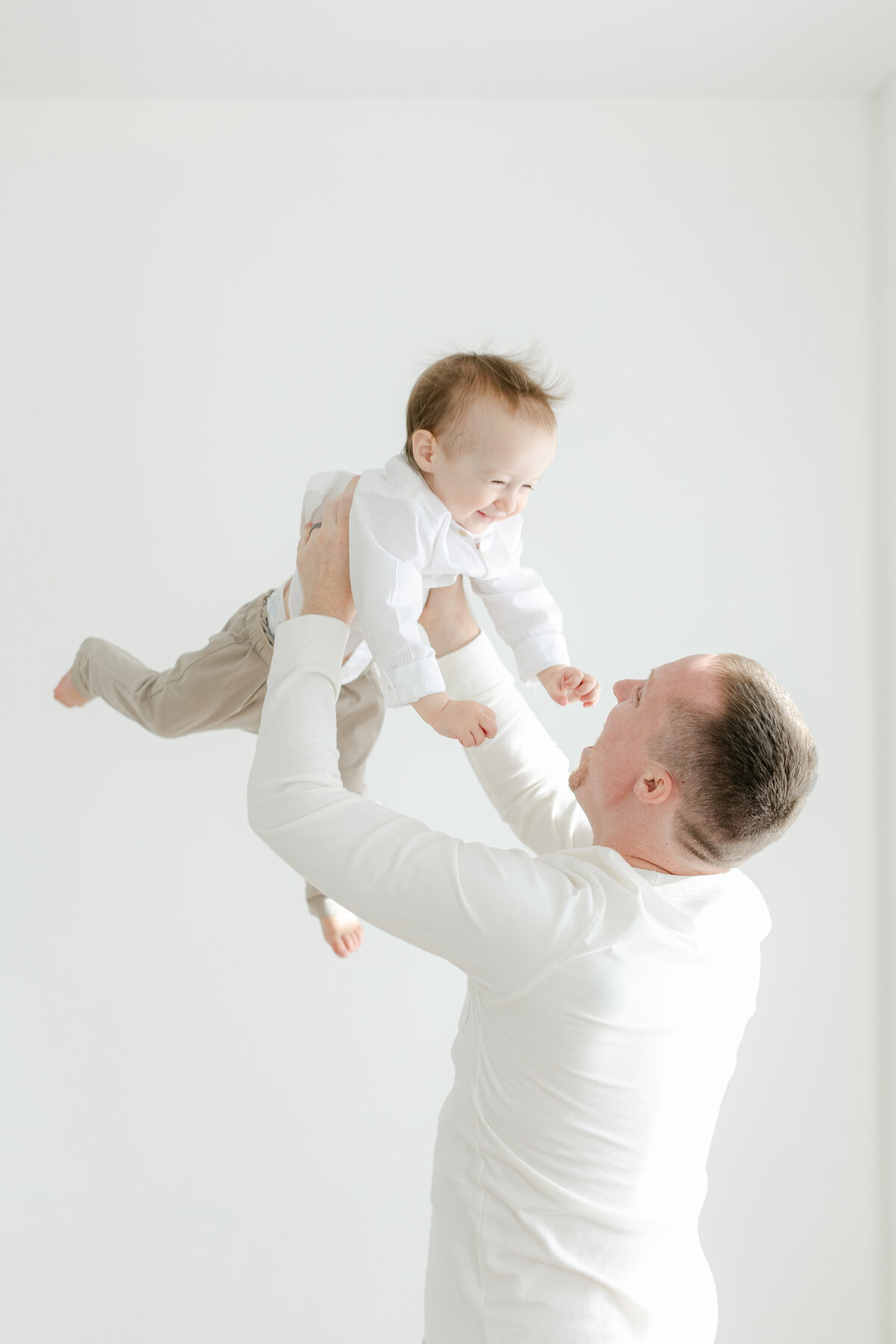 Dad tossing his toddler in the air laughing and playing in Philadelphia Portrait Photographer Tara Federico's haddonfield NJ studio
