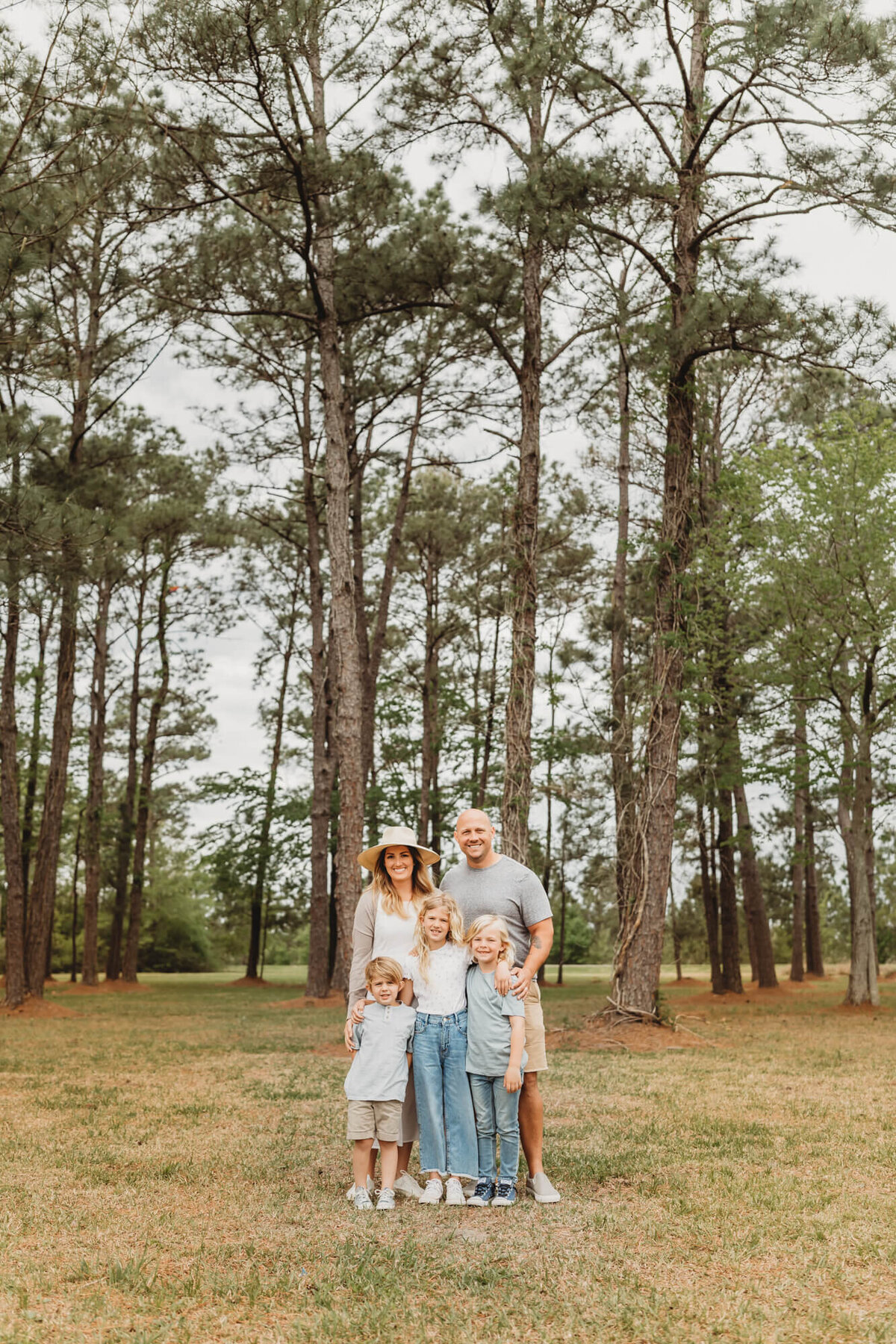 family stands in front of tall pine trees at a park in Houston Texas.