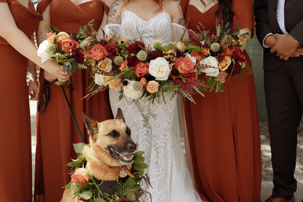 Burgundy, peach, orange, and white bouquets held by bridesmaids in dark orange dresses.