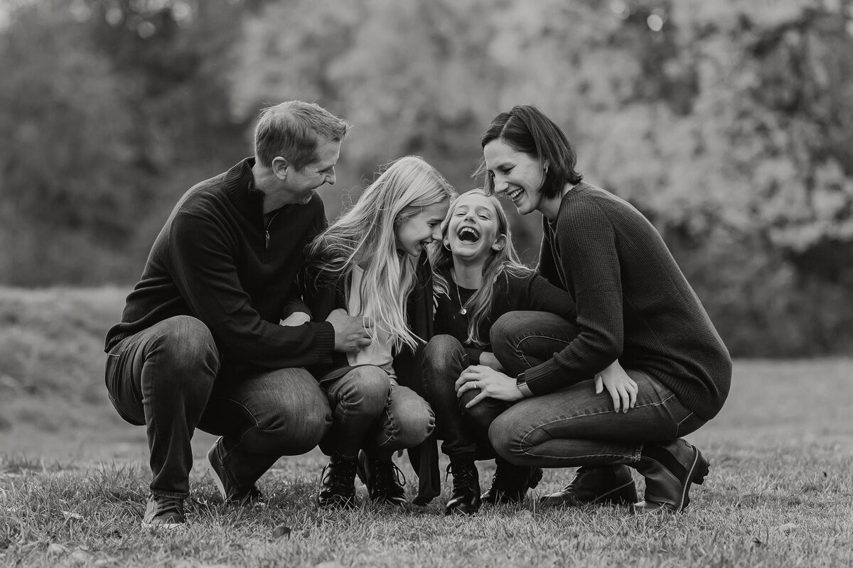 Family squatting down and laughing together, sharing a fun and lighthearted moment during their lifestyle photo session.