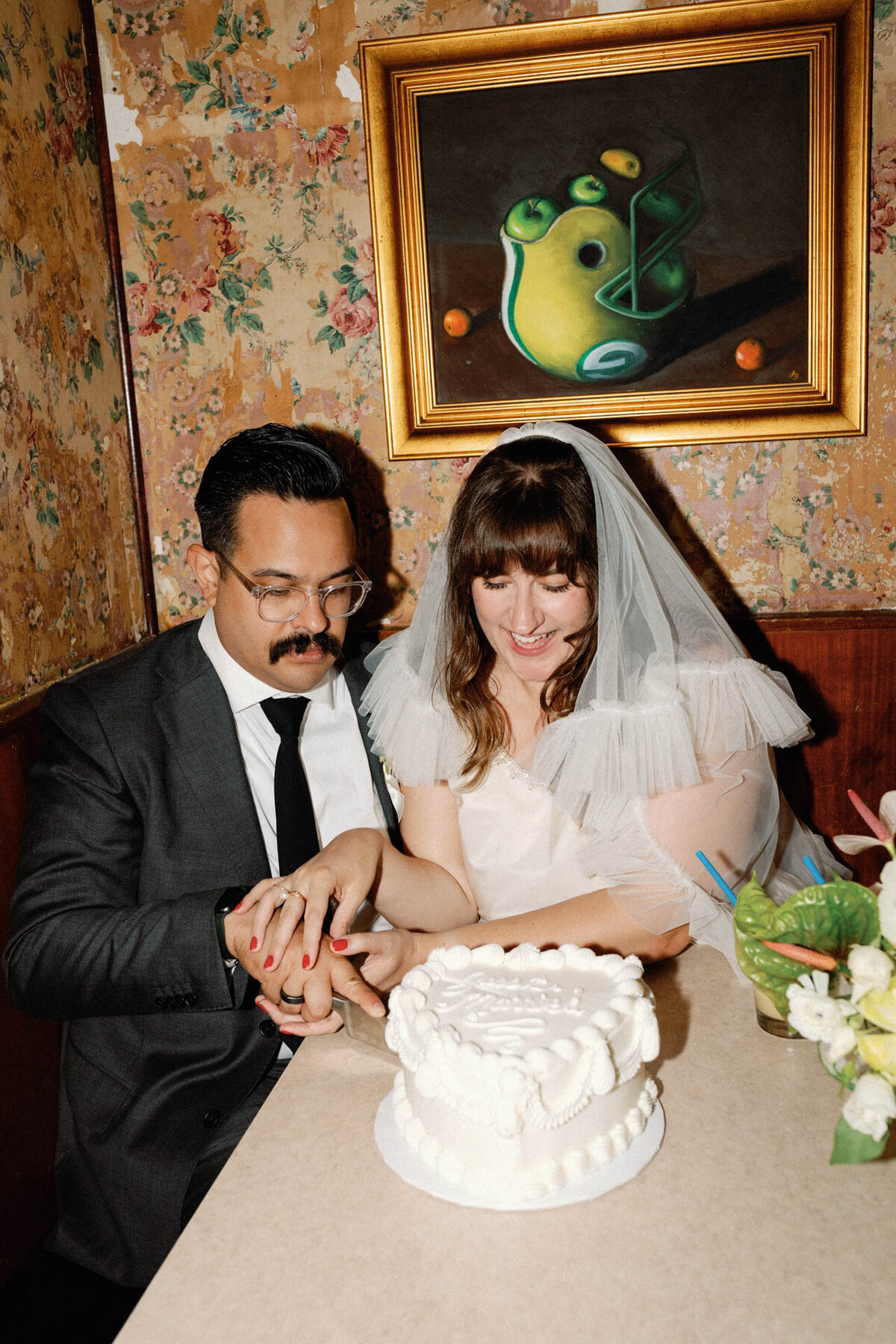 Brooklyn intimate wedding reception at Long Island Bar cutting heart shaped retro white cake with floral wallpaper in booth