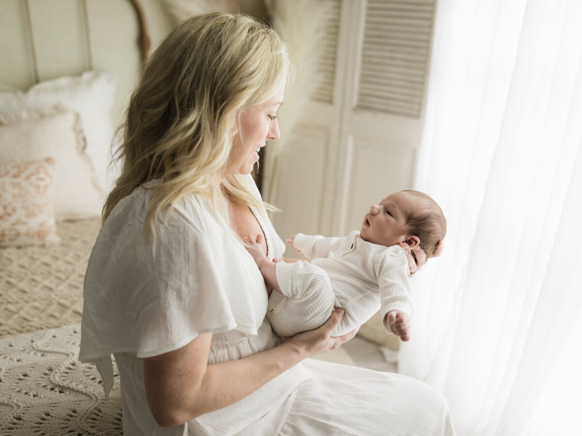 mom holding newborn baby boy in white onesie for studio photoshoot 