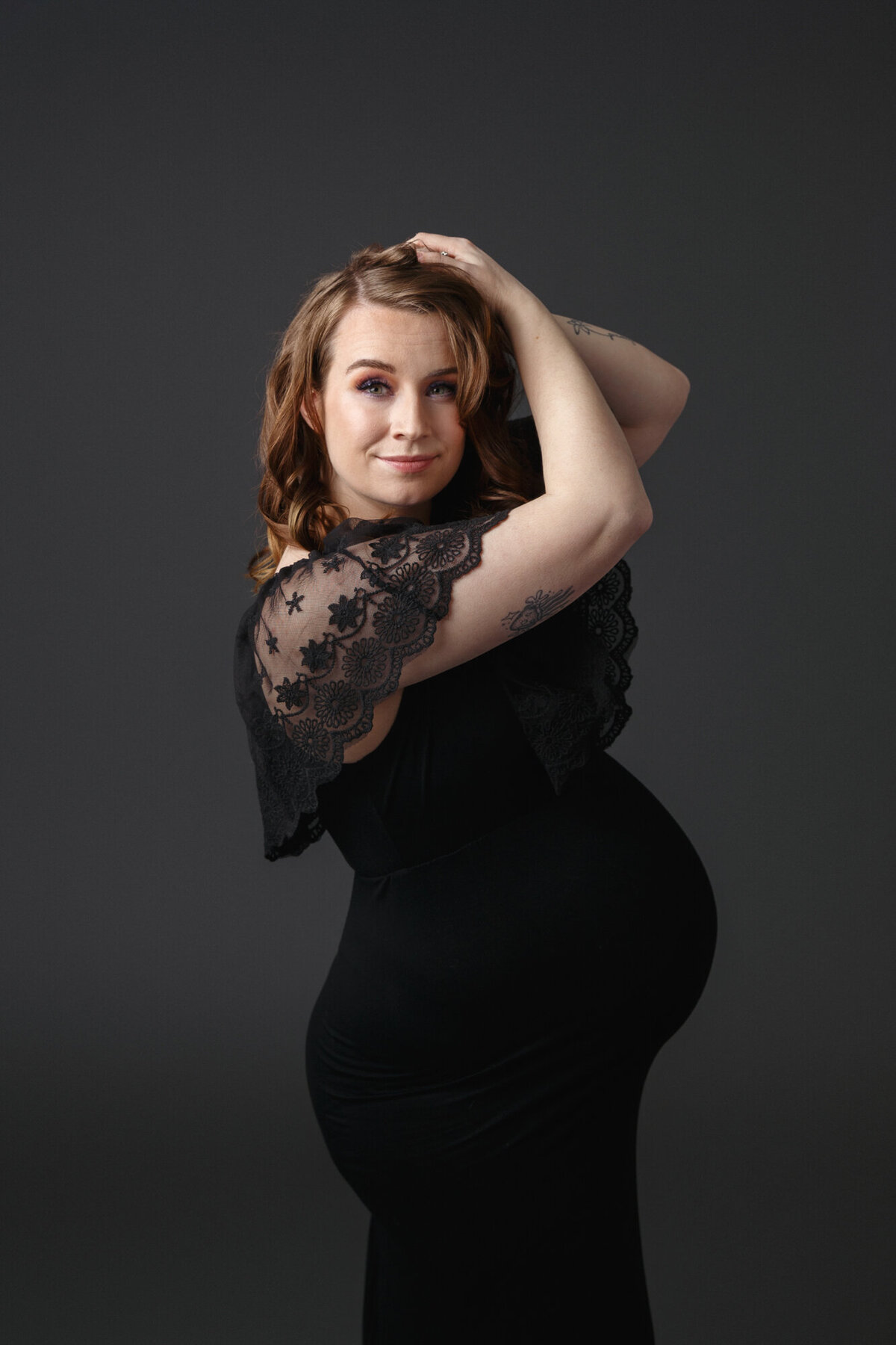 Professional portrait of a beautiful pregnant woman wearing a black dress with lace sleeves