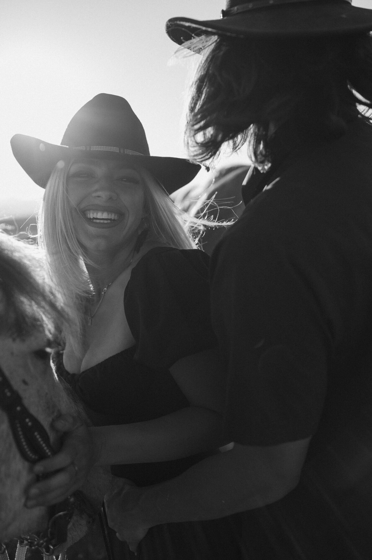 sunset engagement session with couple laughing while their horse calmly standing by their side