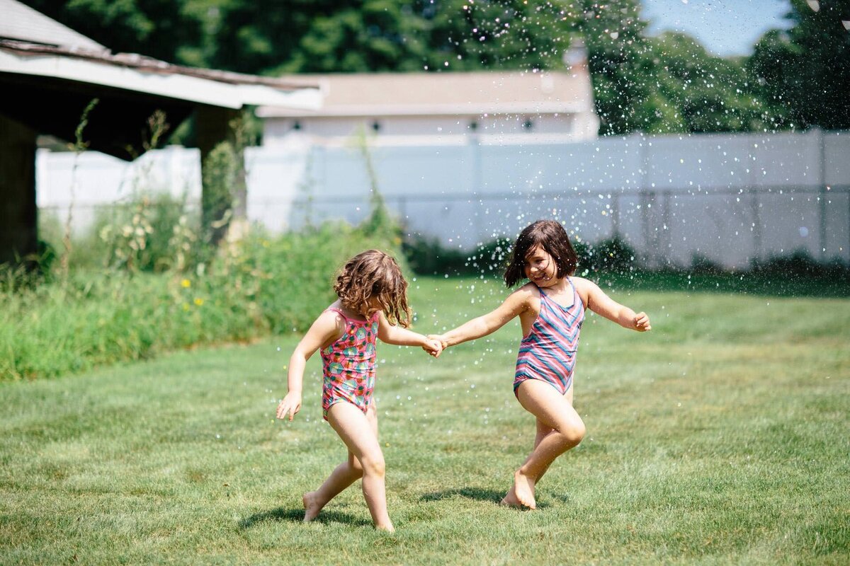 summer family portrait of sisters running through the sprinklers