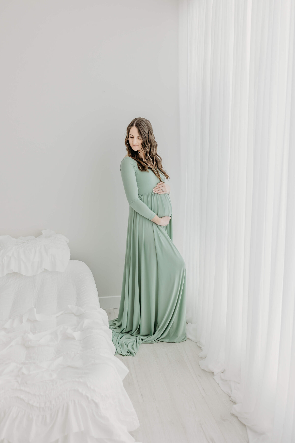 All white studio with pregnant mom in long flowy green dress near Eau Claire Wisconsin
