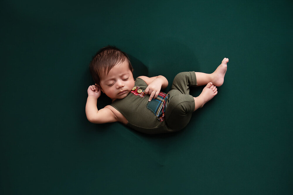 Newborn boy wearing a green outfit in a heart background for his Hamilton newborn photography session.