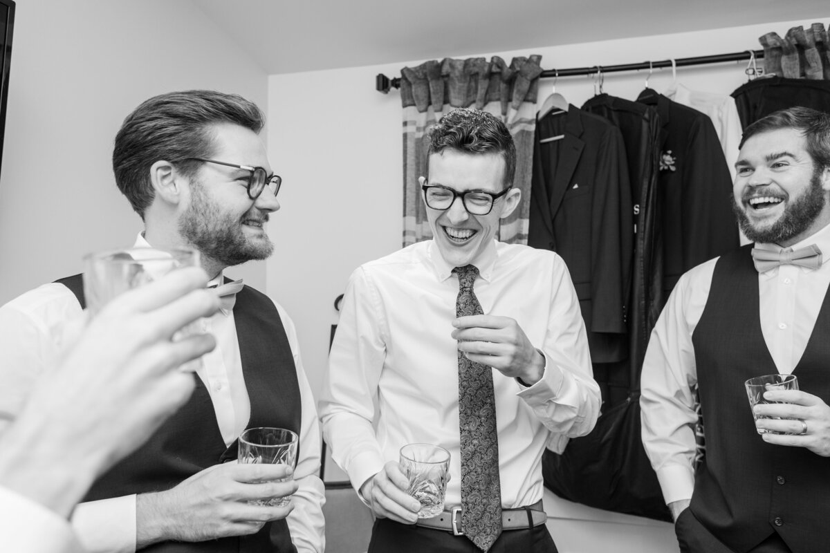 A Groom laughs while doing a shot with his groomsmen on his wedding day in Boone, NC