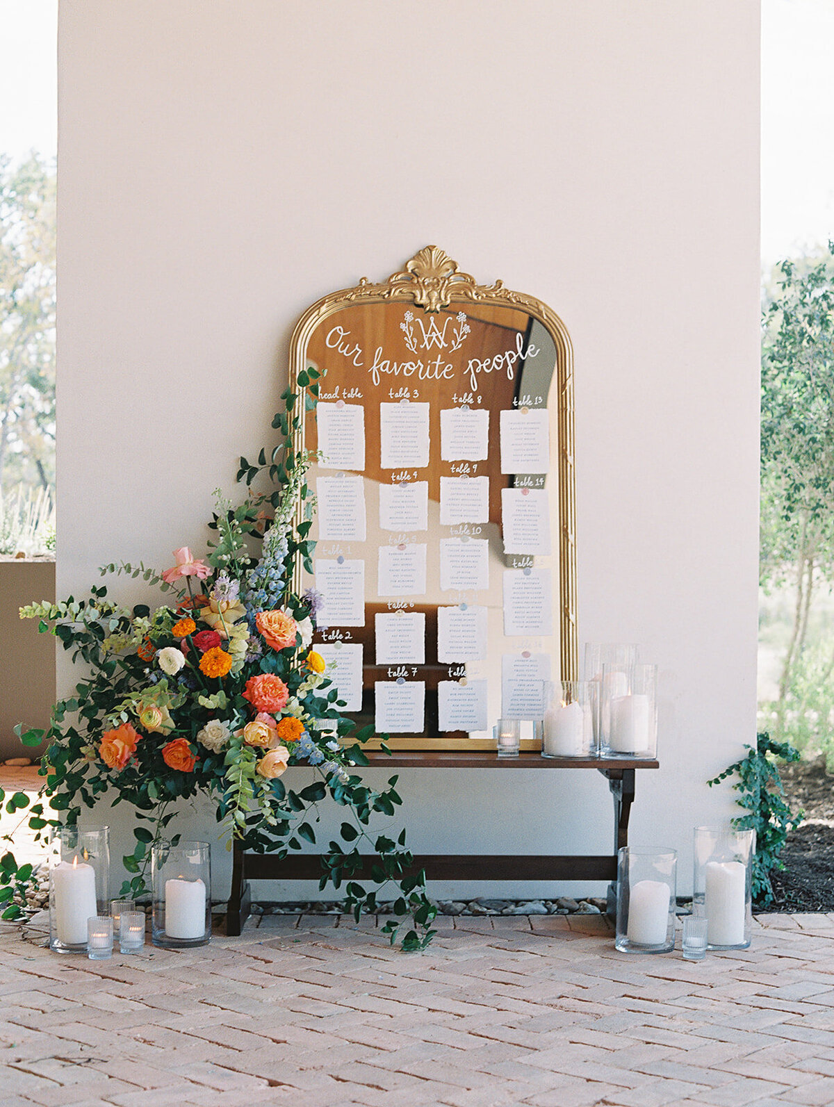 A mirror has been turned into an escort card display as it sits on a bench with flowers