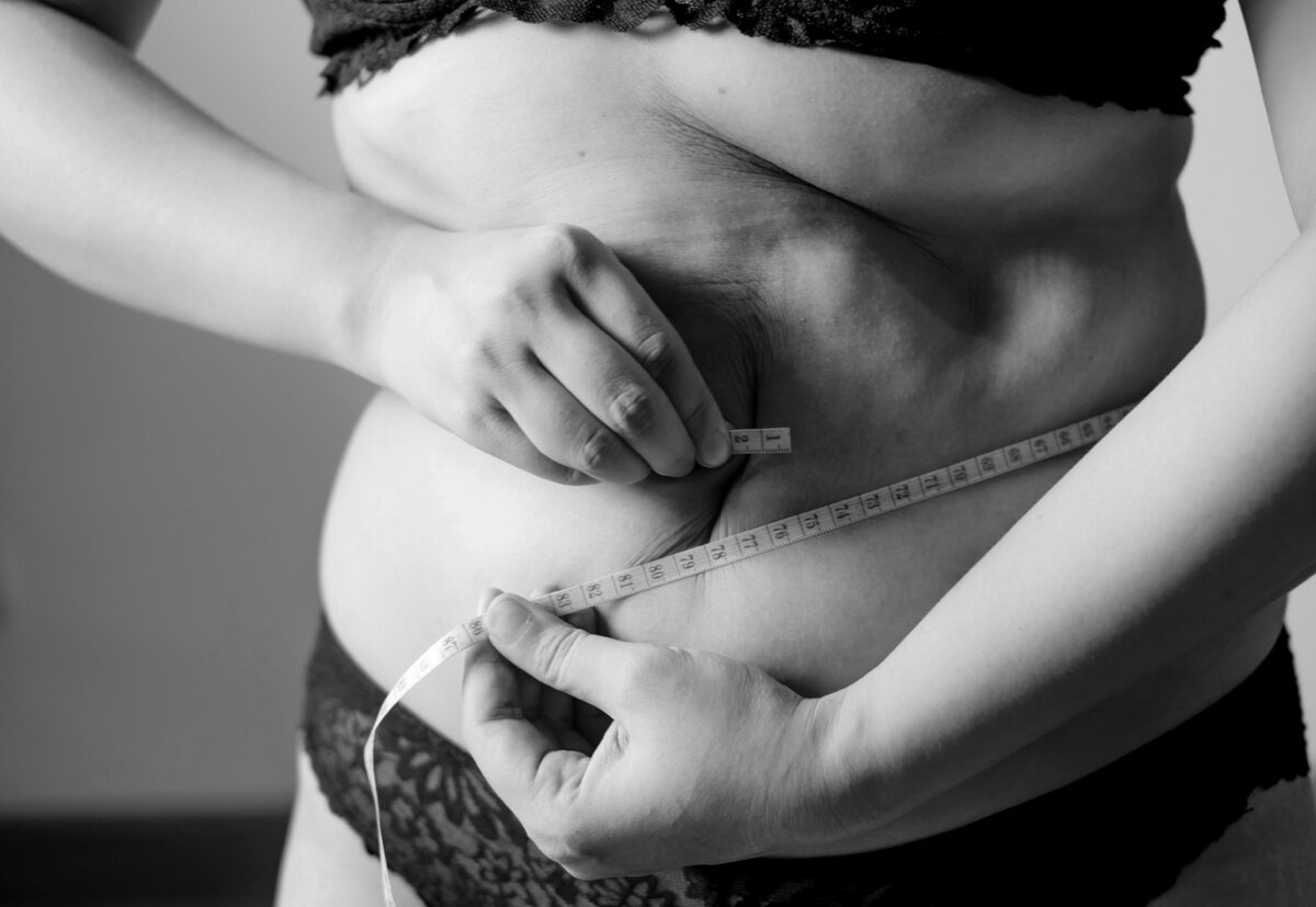 Black and white image capturing a woman measuring her waist with a tape measure, underscoring a moment of personal health assessment in Charlotte Hunter's Menopause Midsection Makeover journey.