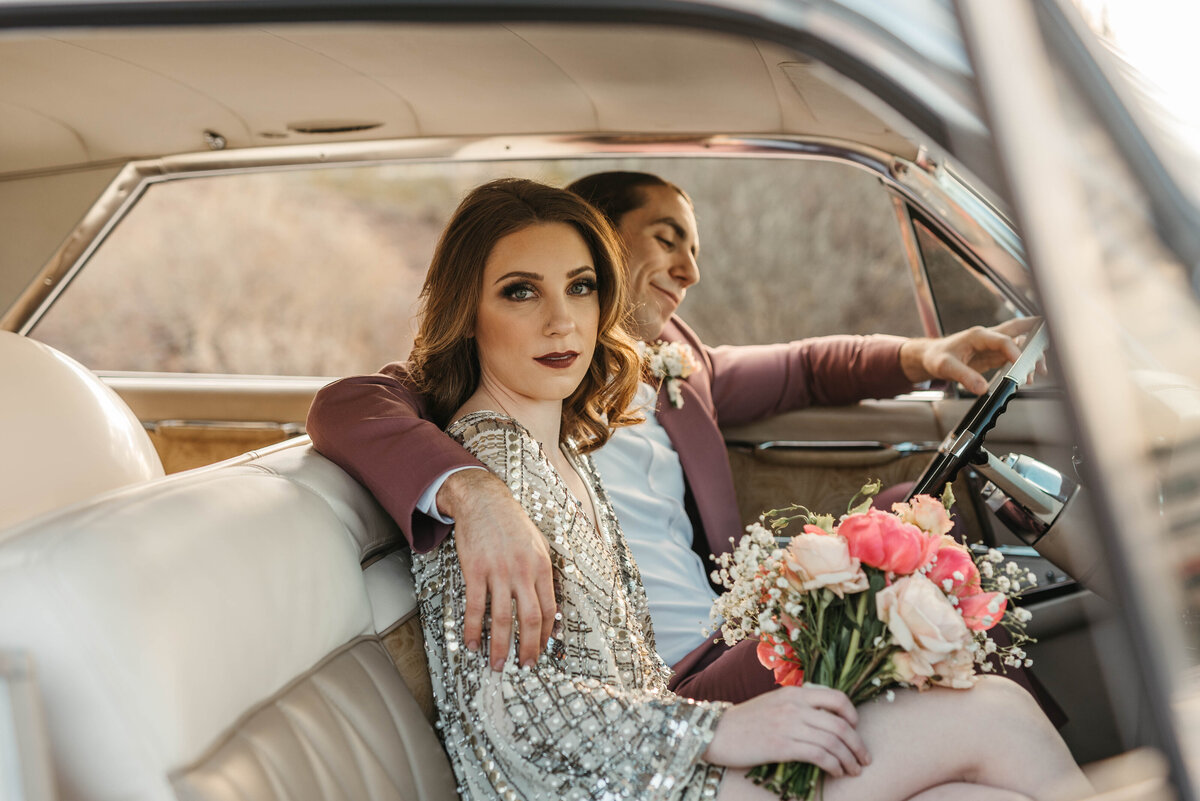 A bride and groom sit in vintage car