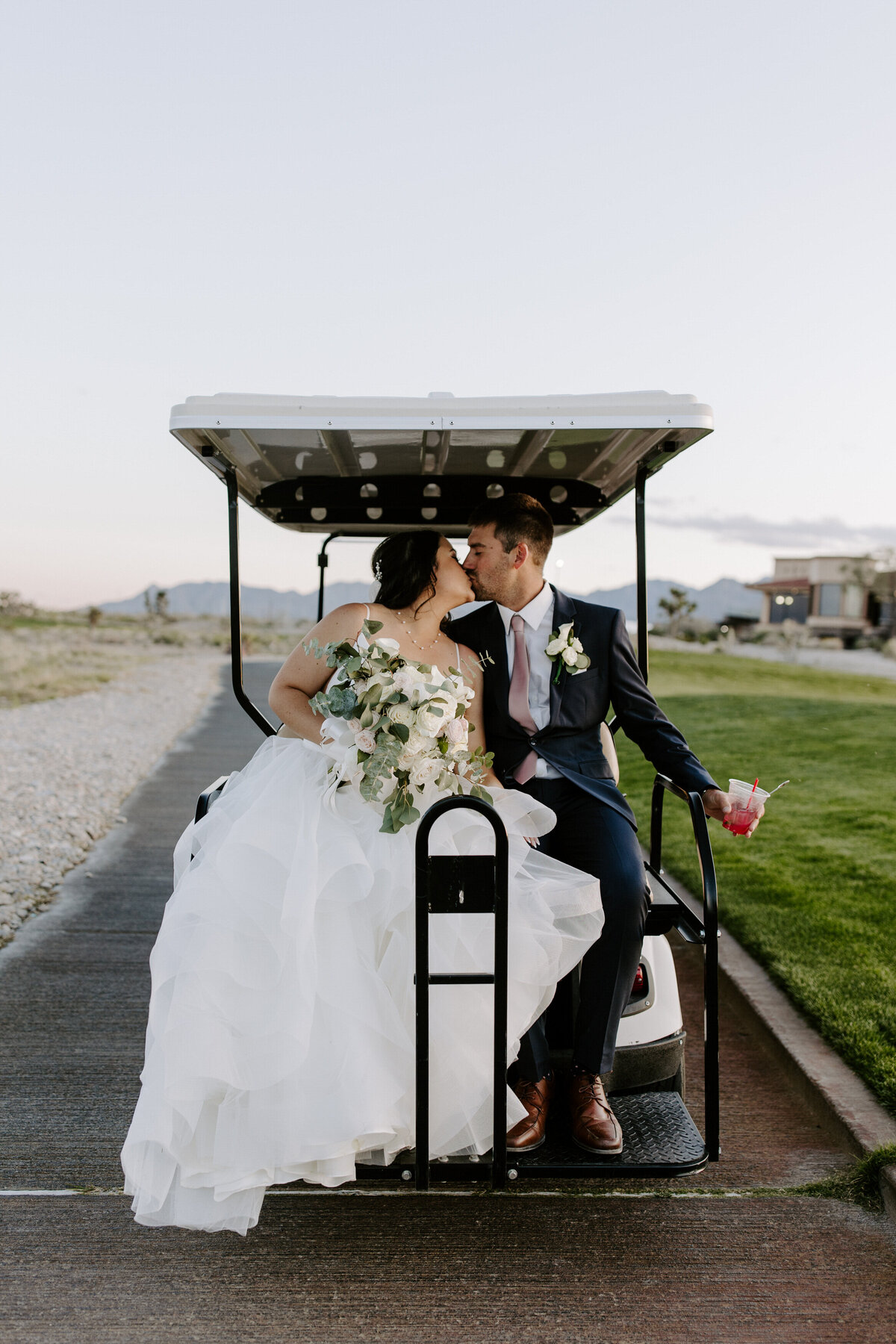 A couple kisses on the back of a golf cart on their wedding day.