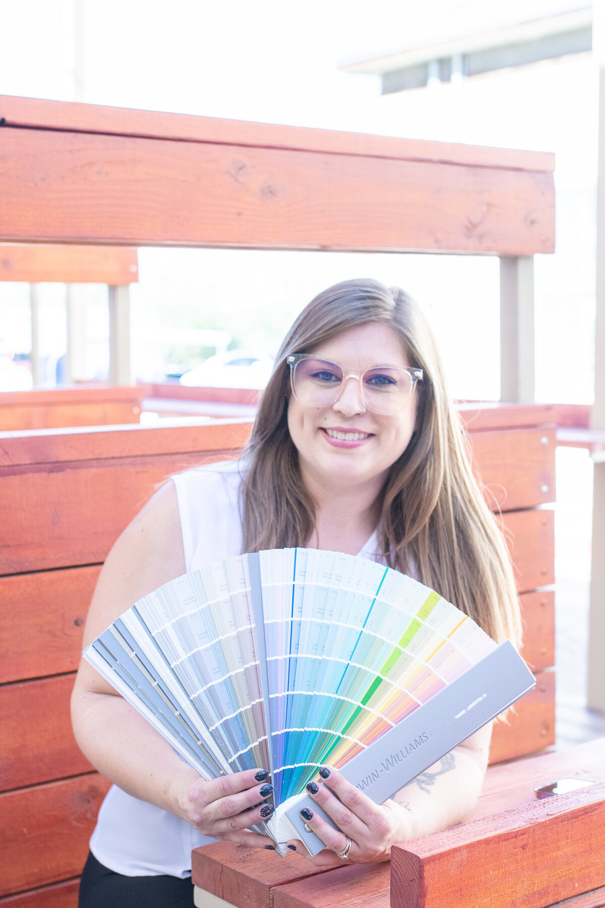 Woman smiling and holding a large Sherwin-Williams color fan deck while sitting outdoors, photographed by Vyrl Photo, showcasing Tucson brand photography.