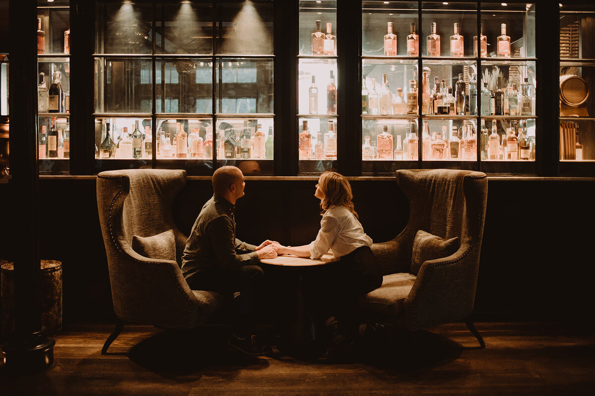A couple sitting in lounge chairs holding hands over a small table 