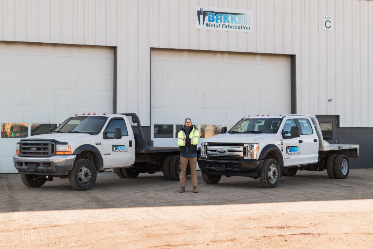 man standing in front of two work trucks outside of company building