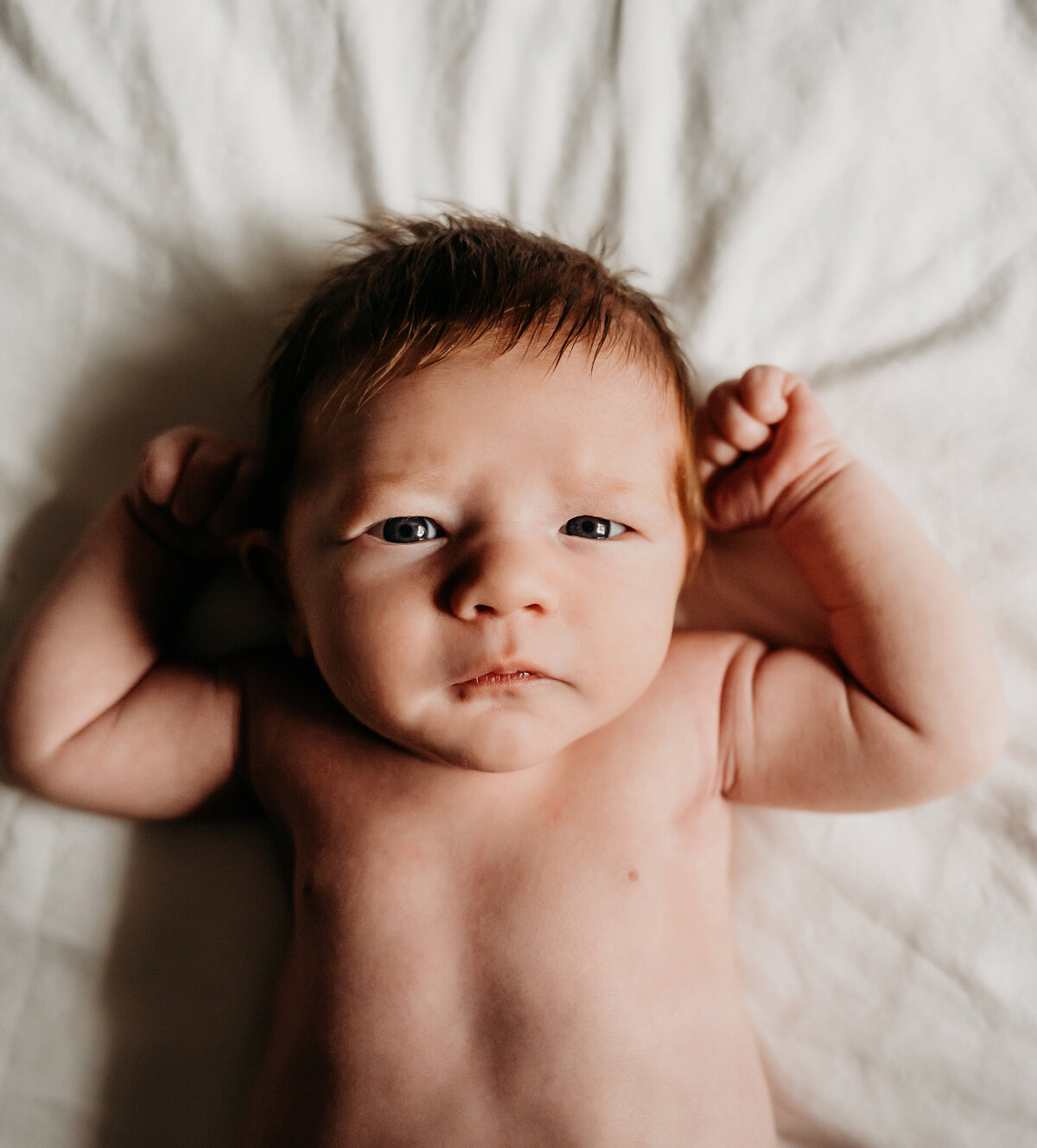 Newborn Photographer, a little baby boy lays on the bed with his arms at his head