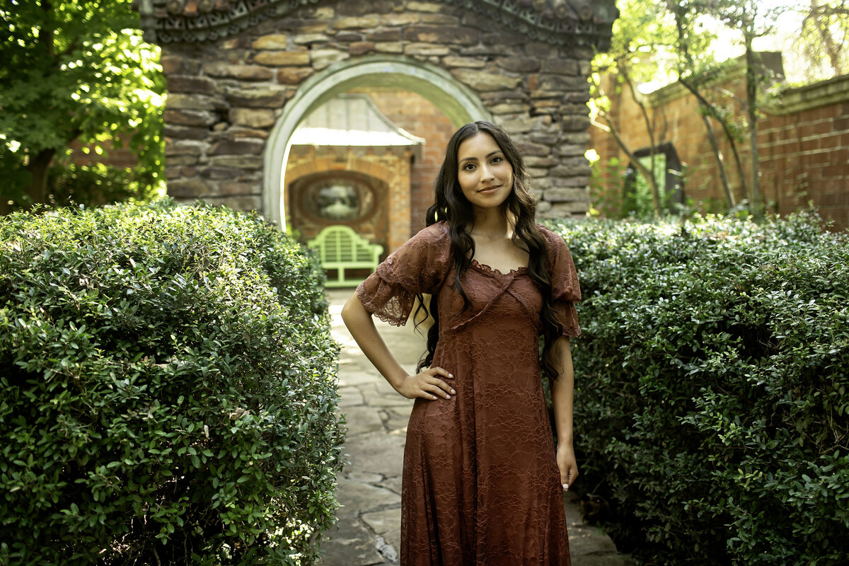 A senior standing confidently by the stone walls and lush green foliage at Chandor Gardens, symbolizing strength, beauty, and the future ahead
