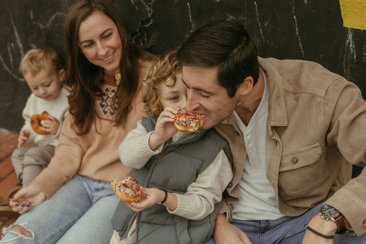 A little boy gives his daddy a bite of his sprinkled donut. 