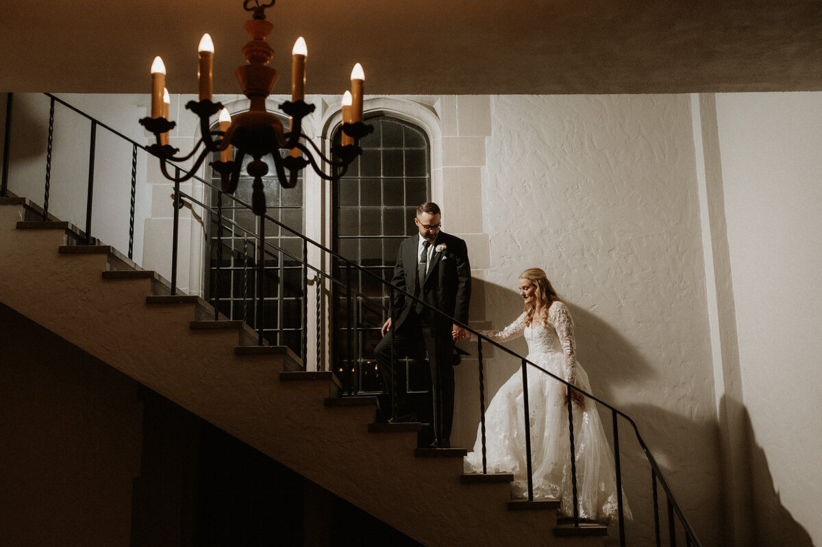 Bride and groom walking down the staircase at Trinity Church during their Michigan City wedding, captured by Rainstorm Photo & Video with warm, cinematic light and documentary-style storytelling.