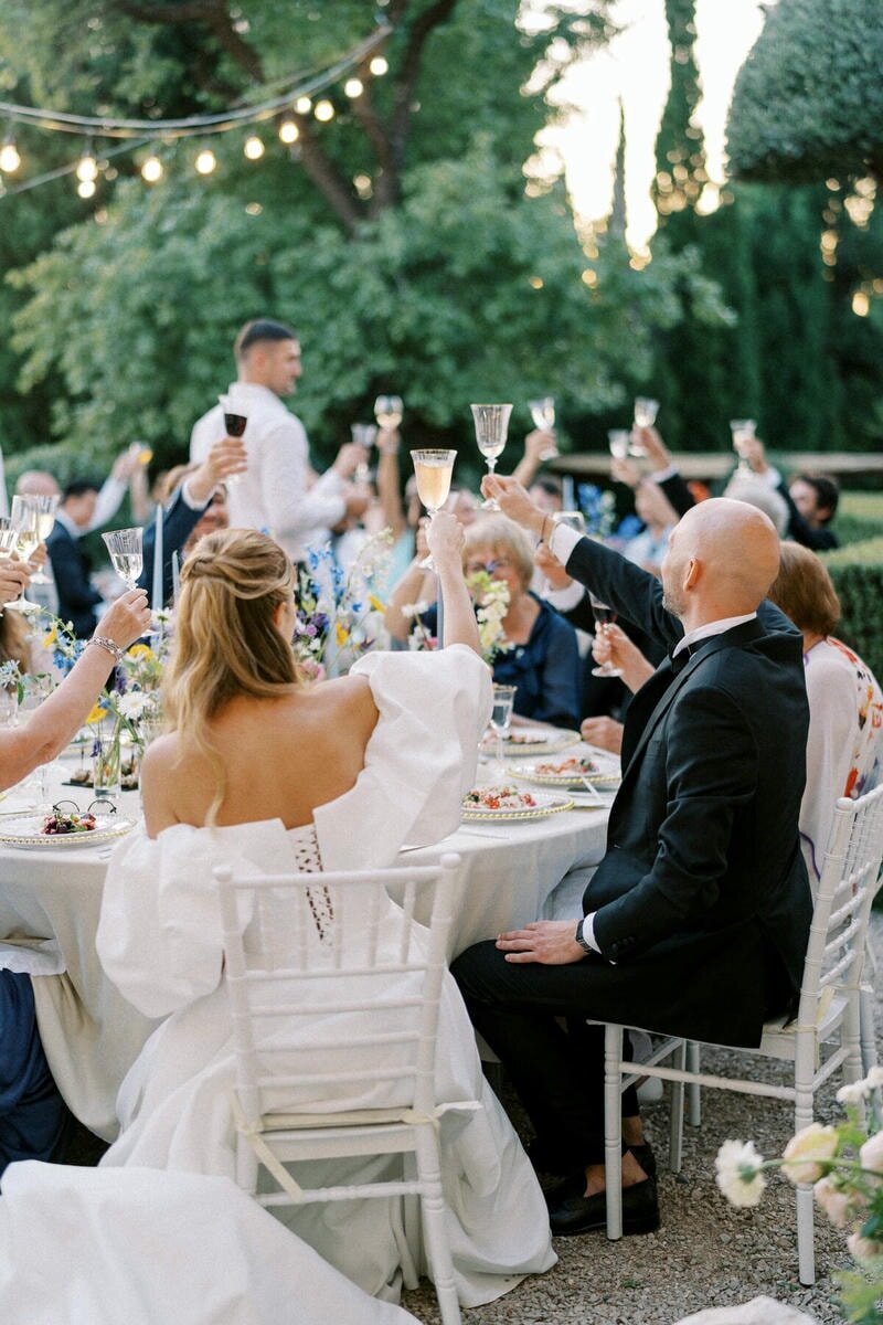 Candid moment of guests raising glasses during an outdoor wedding dinner celebration, captured by Toronto wedding photographer Nadtochiy