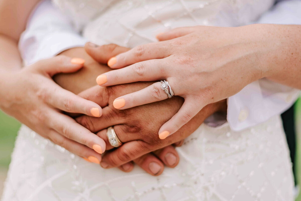 Groom has his hands in front of bride. Bride has her hands ontop of grooms. Close up image of their hands.