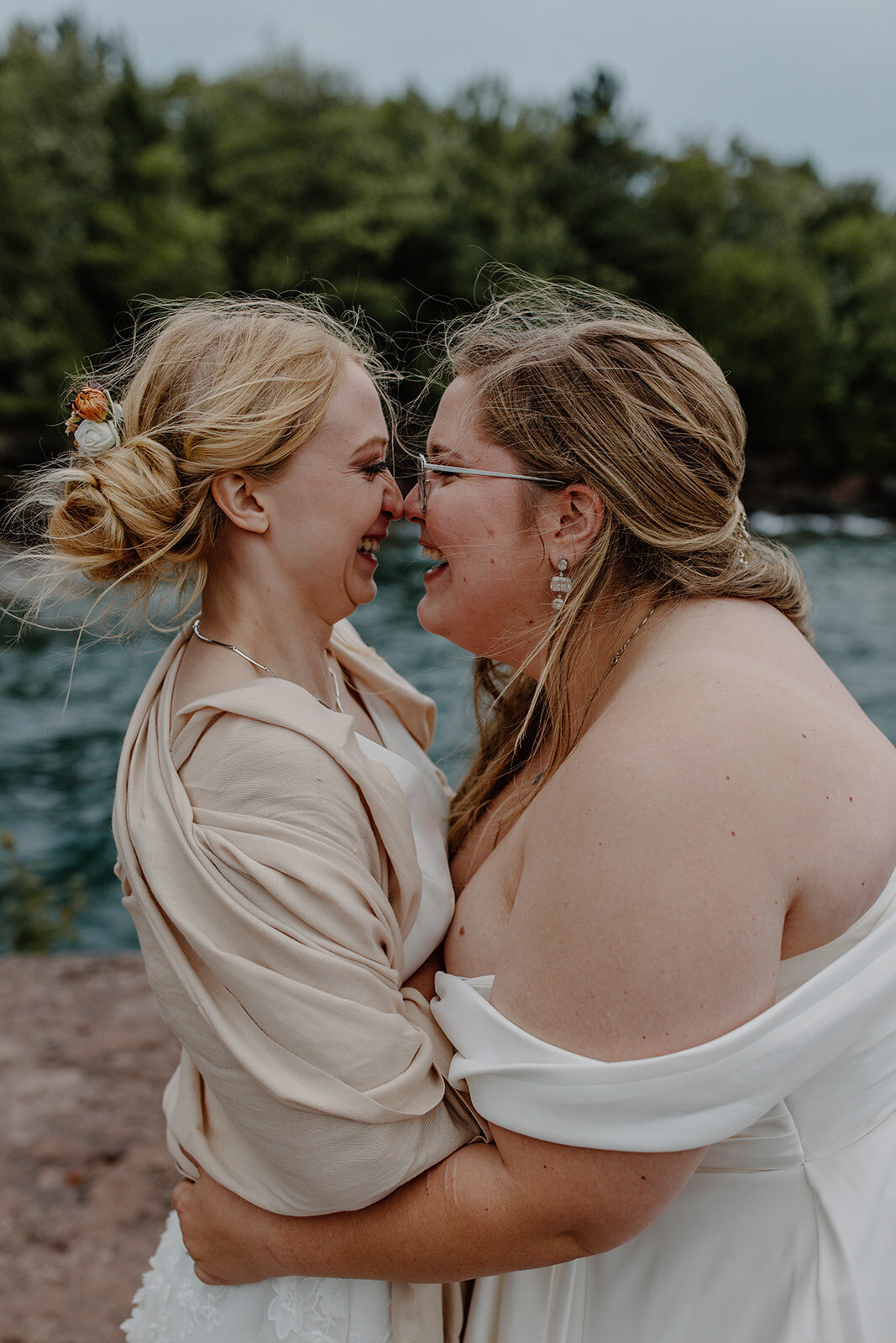 Two brides embracing each other and laughing along the cliffs of Lake Superior in Bay Bay State Park for their Madeline Island elopement